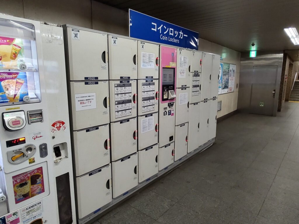 Photo showing a bank of coin lockers in Tokyo's Hanzomon Station, adjacent to signage and stairs, and next to an ice cream vending machine